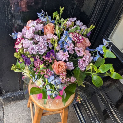 Cottage Garden Pastels - A relaxed, garden-gathered hand-tie in soft lilac chrysanthemums, sky-blue delphinium, peach roses, purple lisianthus and delicate waxflower. Full of natural country charm.