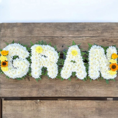 Bespoke Floral Letter Tribute - Personalised funeral lettering created with a base of fresh white flowers, complemented by yellow and orange floral accents and fresh greenery.